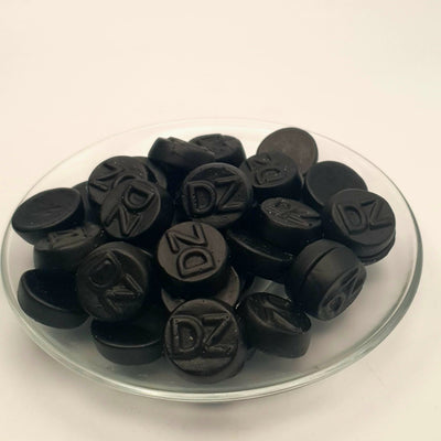 A glass bowl filled with black chocolate chips, enhanced with Letterboxliquorice's DUBBEL ZOUT and licorice extract for a unique twist, creating double salt rounds.