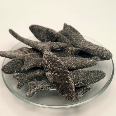 A plate of Letterboxliquorice Sweet and Salty Herrings coated chocolate fish sticks on a white surface.