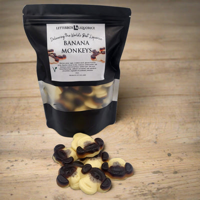 A bag of tasty Letterboxliquorice banana monkeys sitting next to a bag of chocolate.